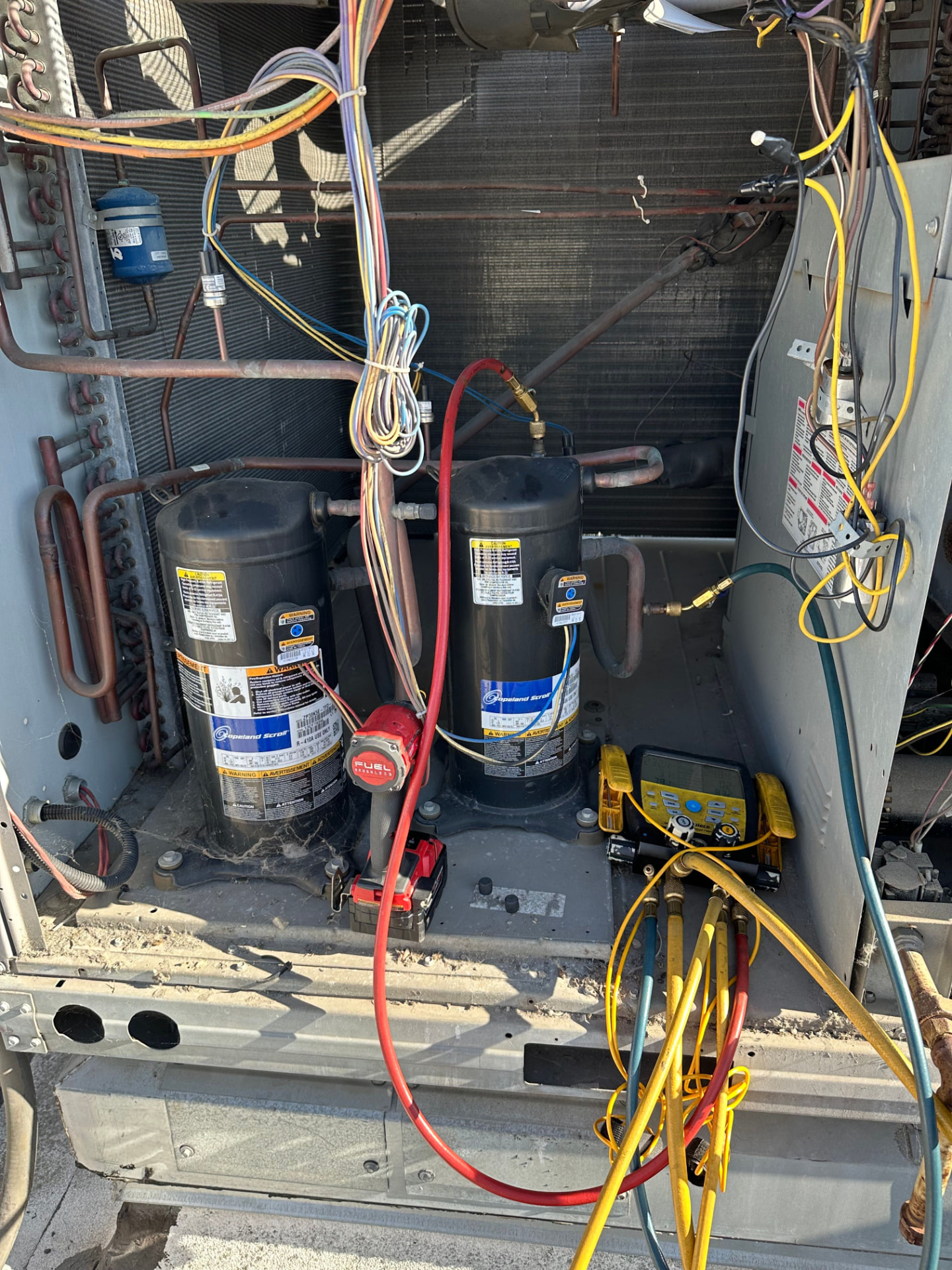 Open rooftop package unit with dual scroll compressors and refrigerant gauges connected during an AC service call