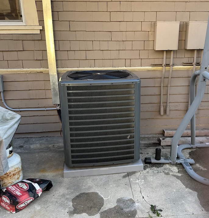 Outdoor air conditioning condenser unit installed on a base against a home exterior